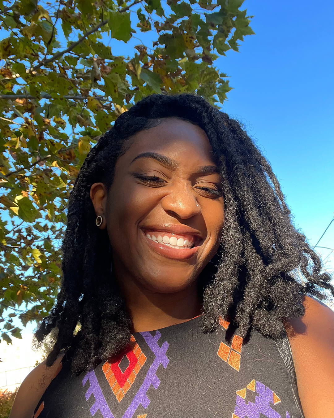 Alexis Moise stands outside, under a tree, smiling at camera